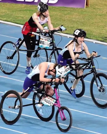 Three athletes competing in Frame Running on a track, each pushing a three-wheeled frame with helmets on, racing side by side.