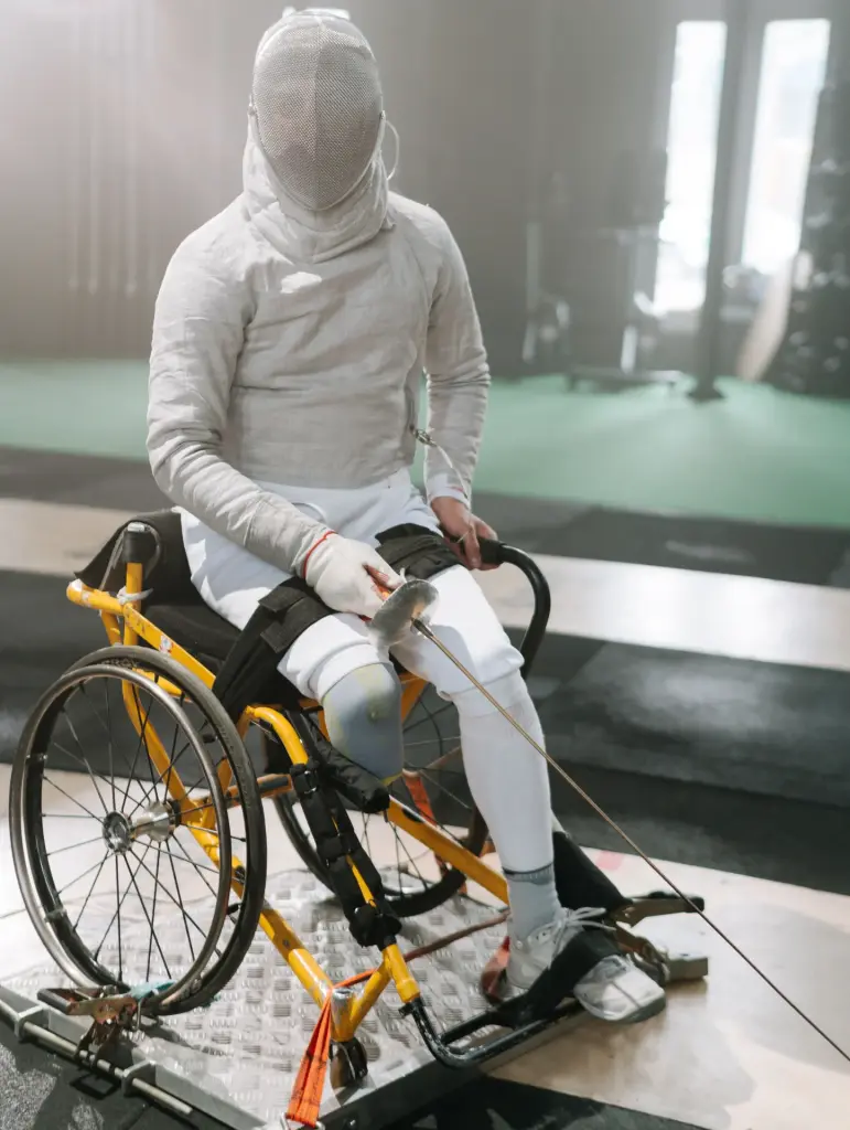 Wheelchair fencer in full protective uniform seated in a specialized sports wheelchair during training.