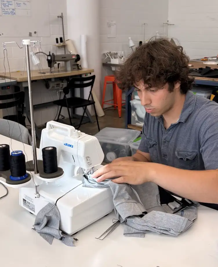RISD industrial design intern Adam Gottesdiener uses a serger sewing machine in the Interwoven studio to construct a grey fabric soft goods prototype.