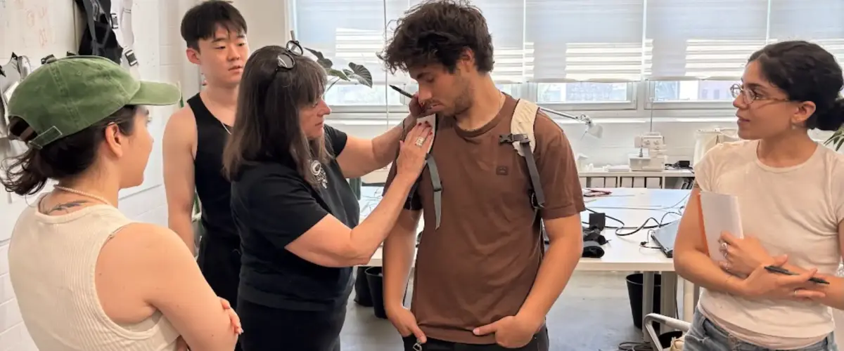 An Interwoven Design leader adjusts a soft goods prototype on an intern in a light-filled industrial design studio, demonstrating mentorship and the design development process for wearable tech.