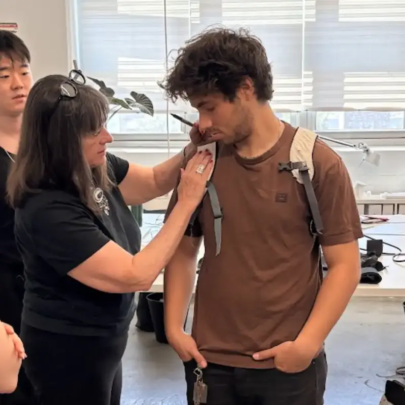 An Interwoven Design leader adjusts a soft goods prototype on an intern in a light-filled industrial design studio, demonstrating mentorship and the design development process for wearable tech.