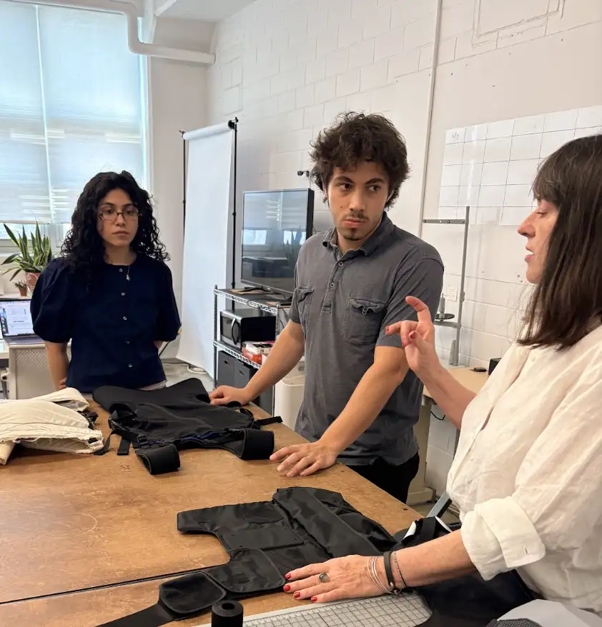 Interwoven Design leadership and interns Adam Gottesdiener and Chloe Bonnet gather around a worktable reviewing black technical soft goods prototypes.