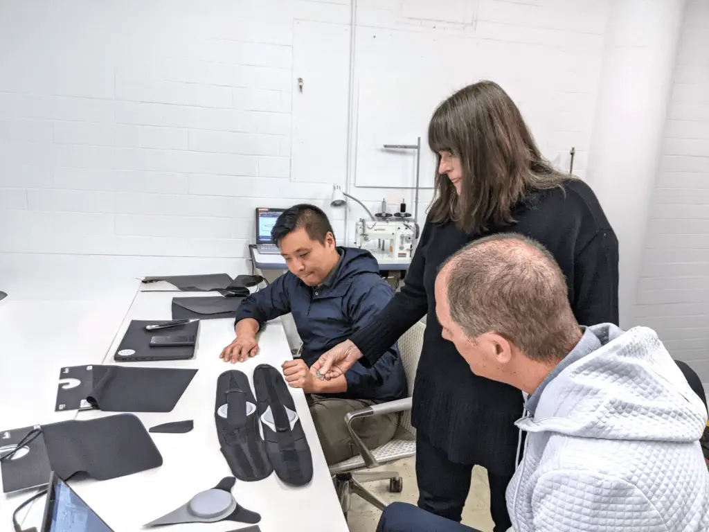 Ivan Lin, Rebeccah Pailes-Friedman, and a collaborator reviewing medical wearable prototypes and textile components at the Interwoven Design studio.